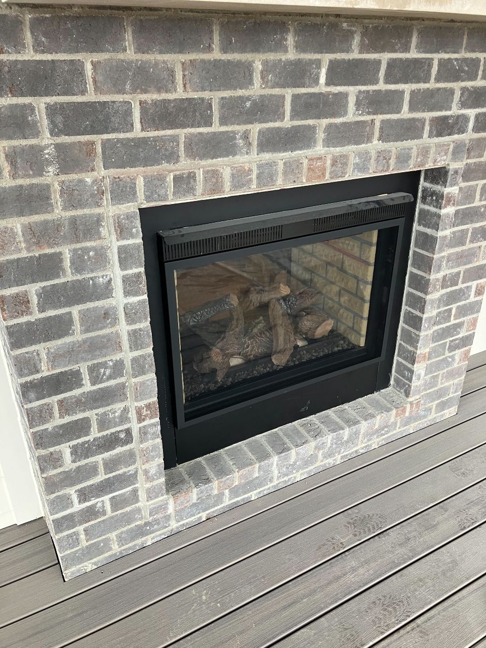 A brick fireplace with a black frame is on a wooden deck.