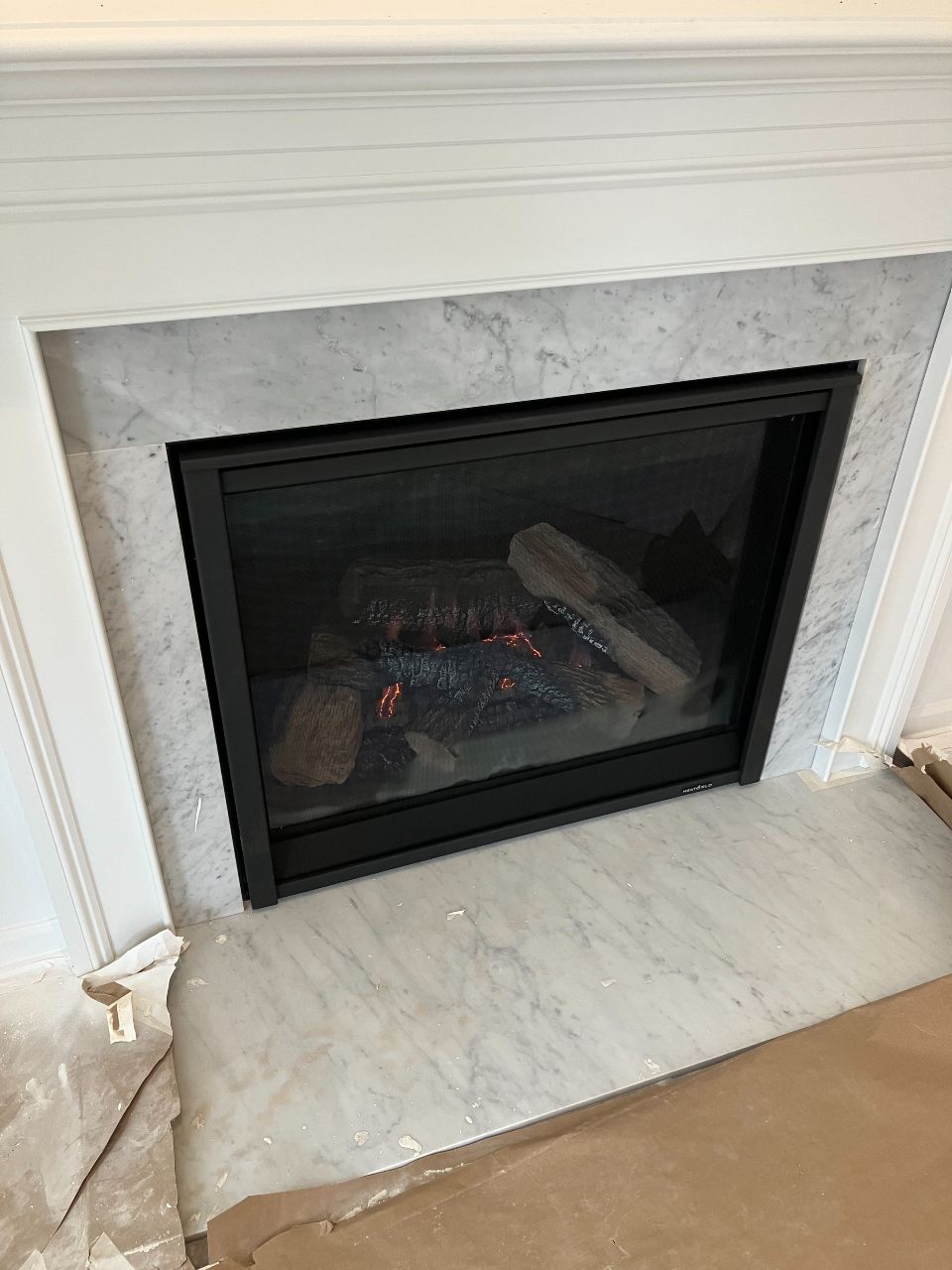 A fireplace with a marble mantle and a glass door is sitting in a living room.