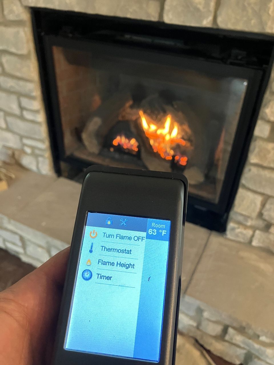 A person is holding a cell phone in front of a fireplace.