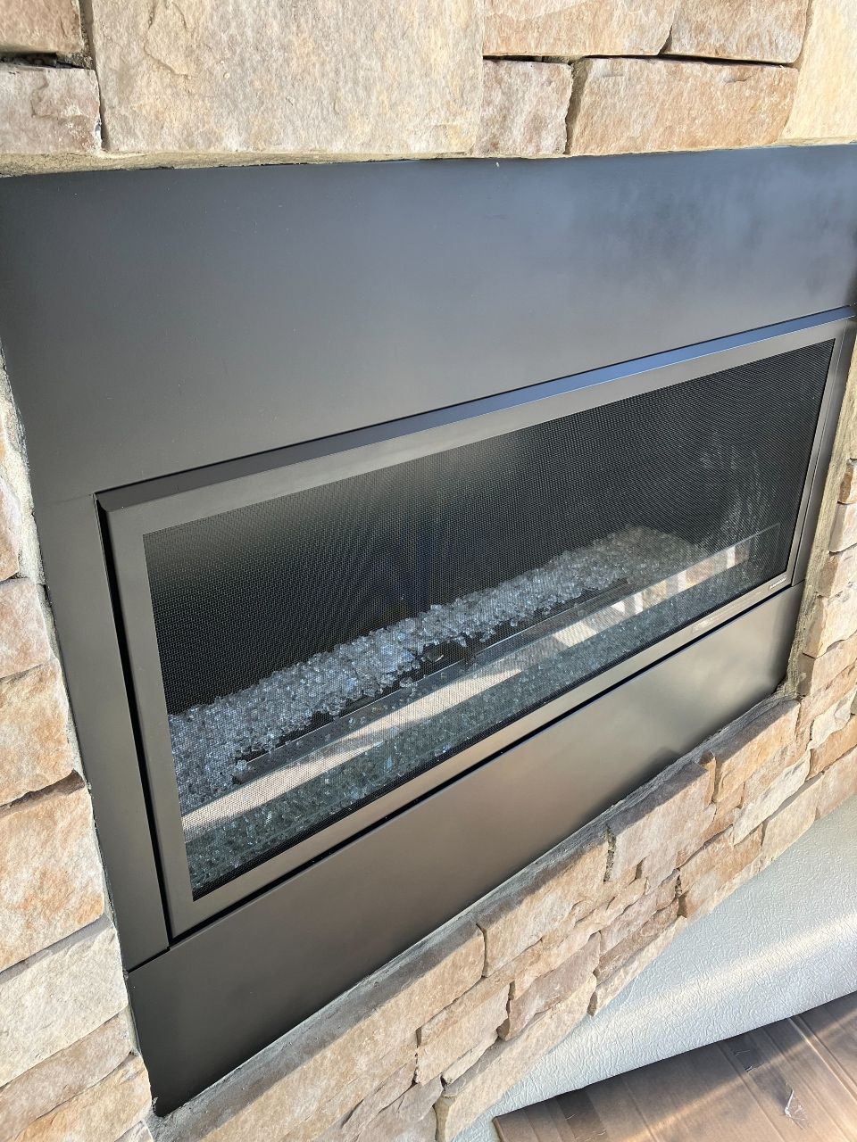 A fireplace is built into a stone wall with a glass door.