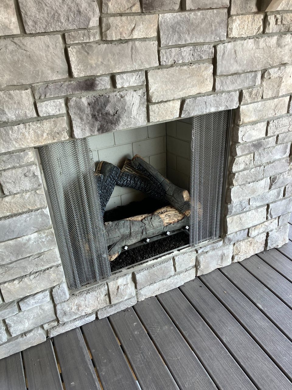 A brick fireplace with logs in it is sitting on a wooden deck.