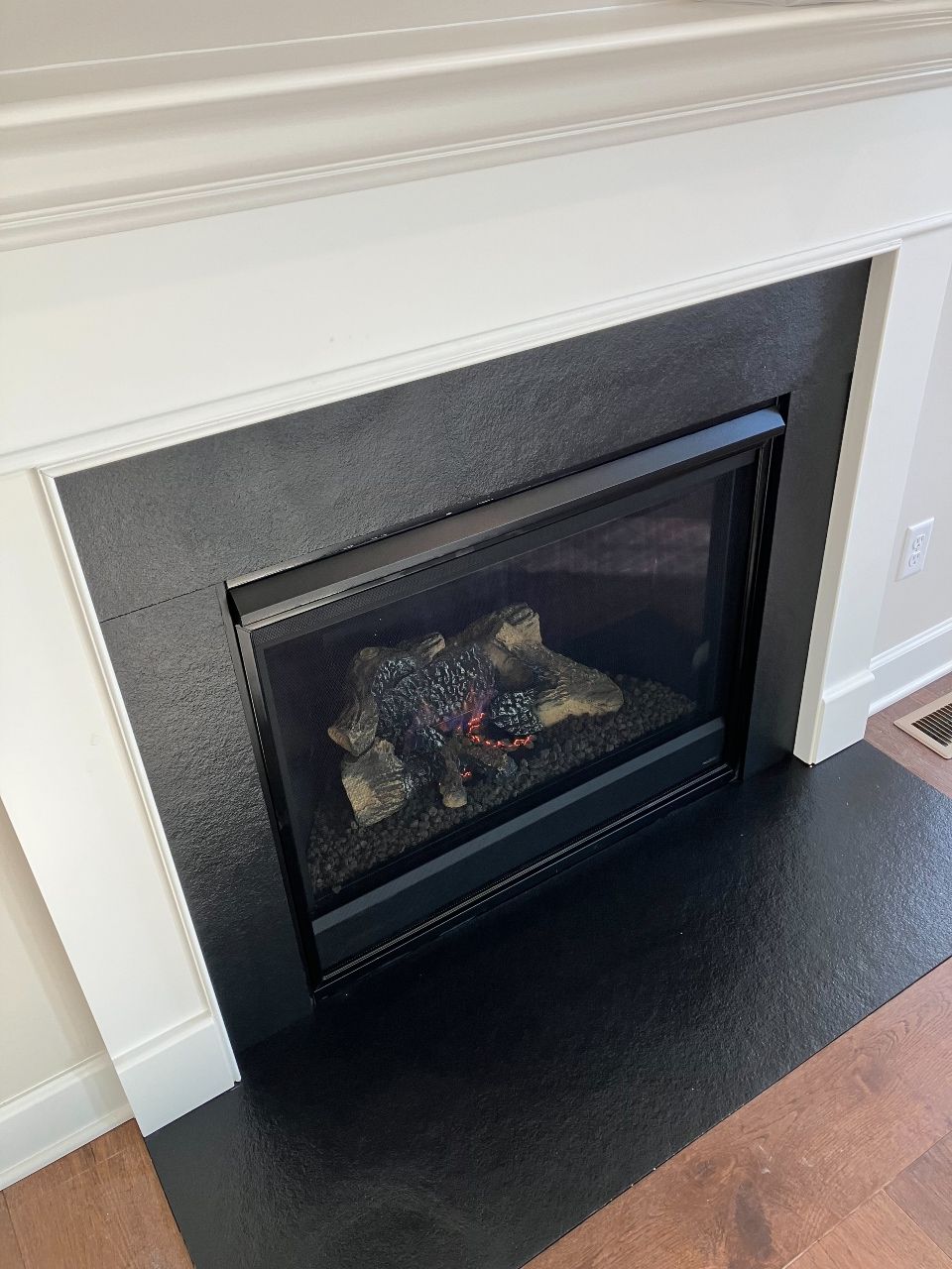 A fireplace with a black tile surround and a white mantle in a living room.