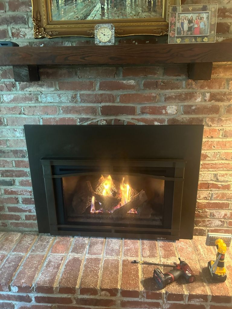 A brick fireplace with a black fireplace insert and a wooden mantle.