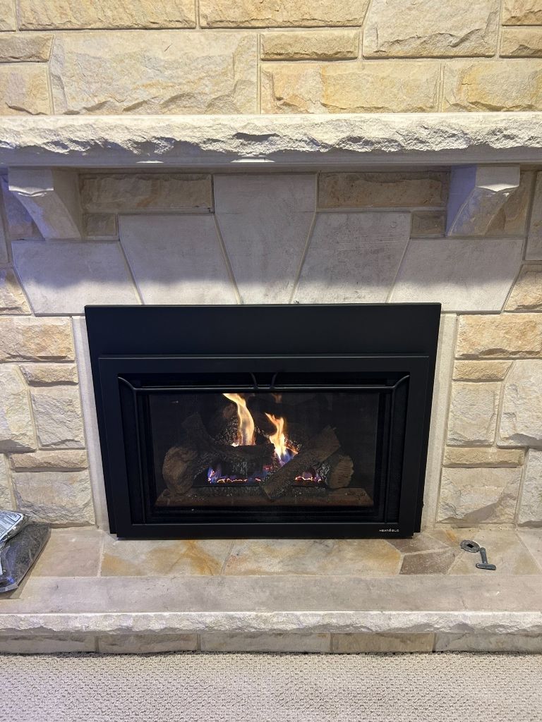 A fireplace with a black insert and a brick mantle.