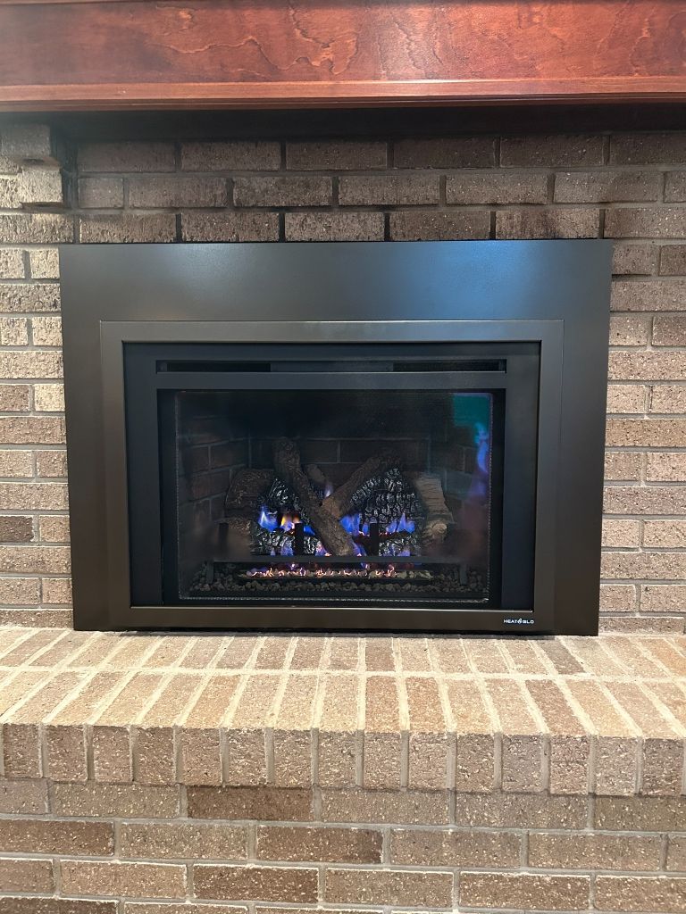 A fireplace with a brick wall and a wooden mantle.