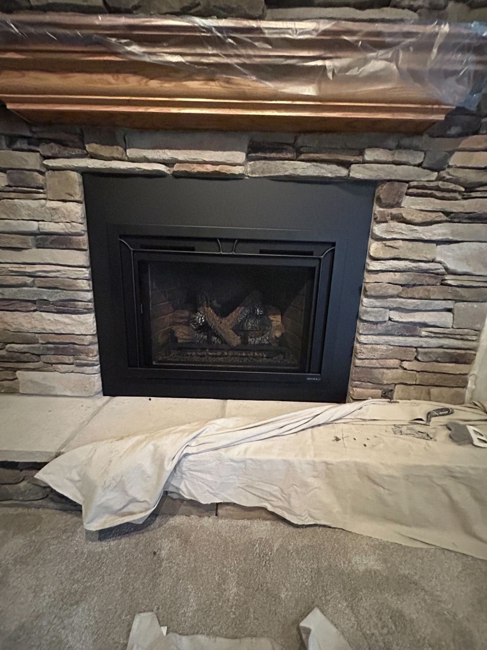 A fireplace with a black trim and a stone wall in a living room.