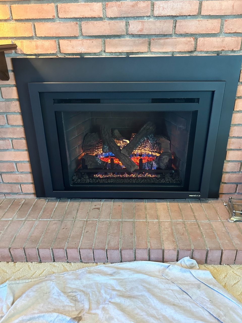 A fireplace with a black frame and a brick wall in a living room.