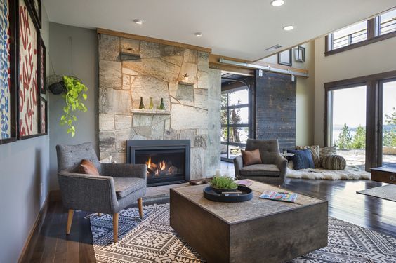 Living room with stone fireplace, armchairs, and large windows overlooking water.