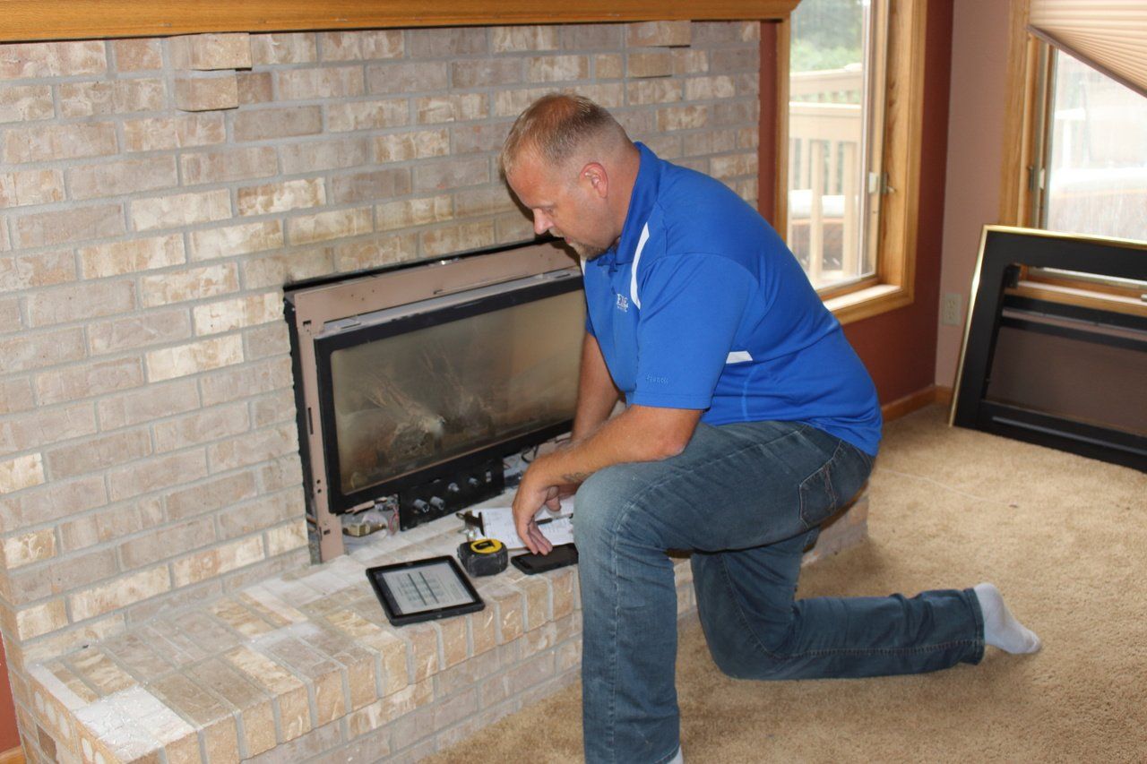 A man in a blue shirt is kneeling down in front of a fireplace.