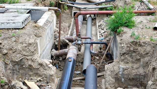 Pipes and other utilities exposed in a trench in the ground, in an outdoor setting.