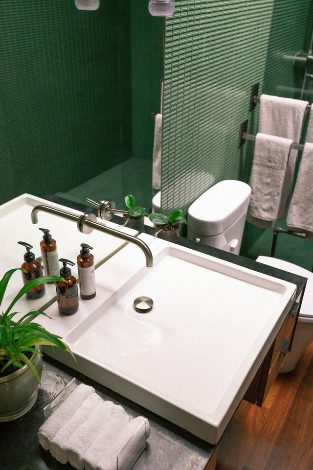 Modern bathroom with green tile walls, white sink, and towels.
