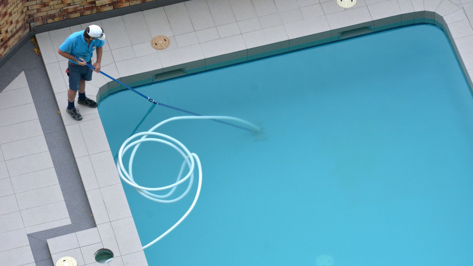A man is cleaning a swimming pool with a hose