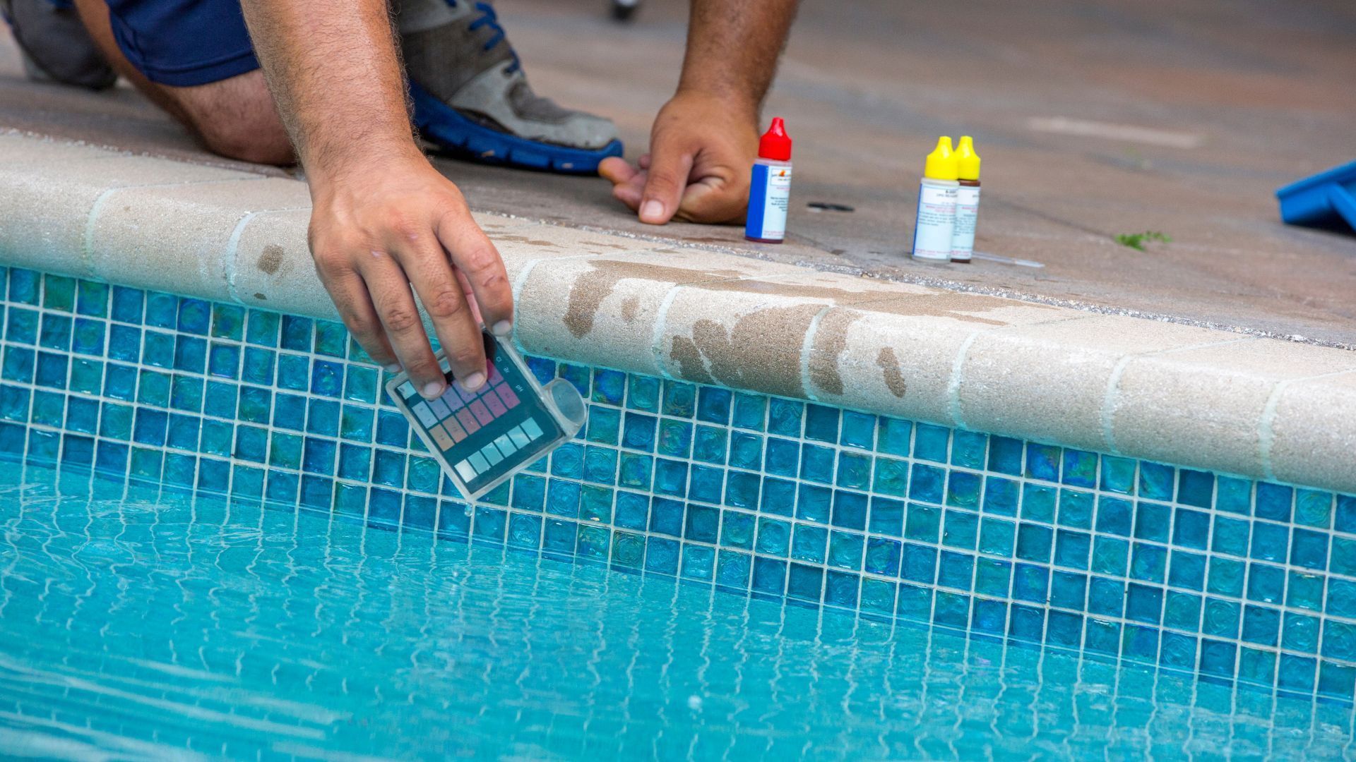 A man is taking a test of the water in a swimming pool.