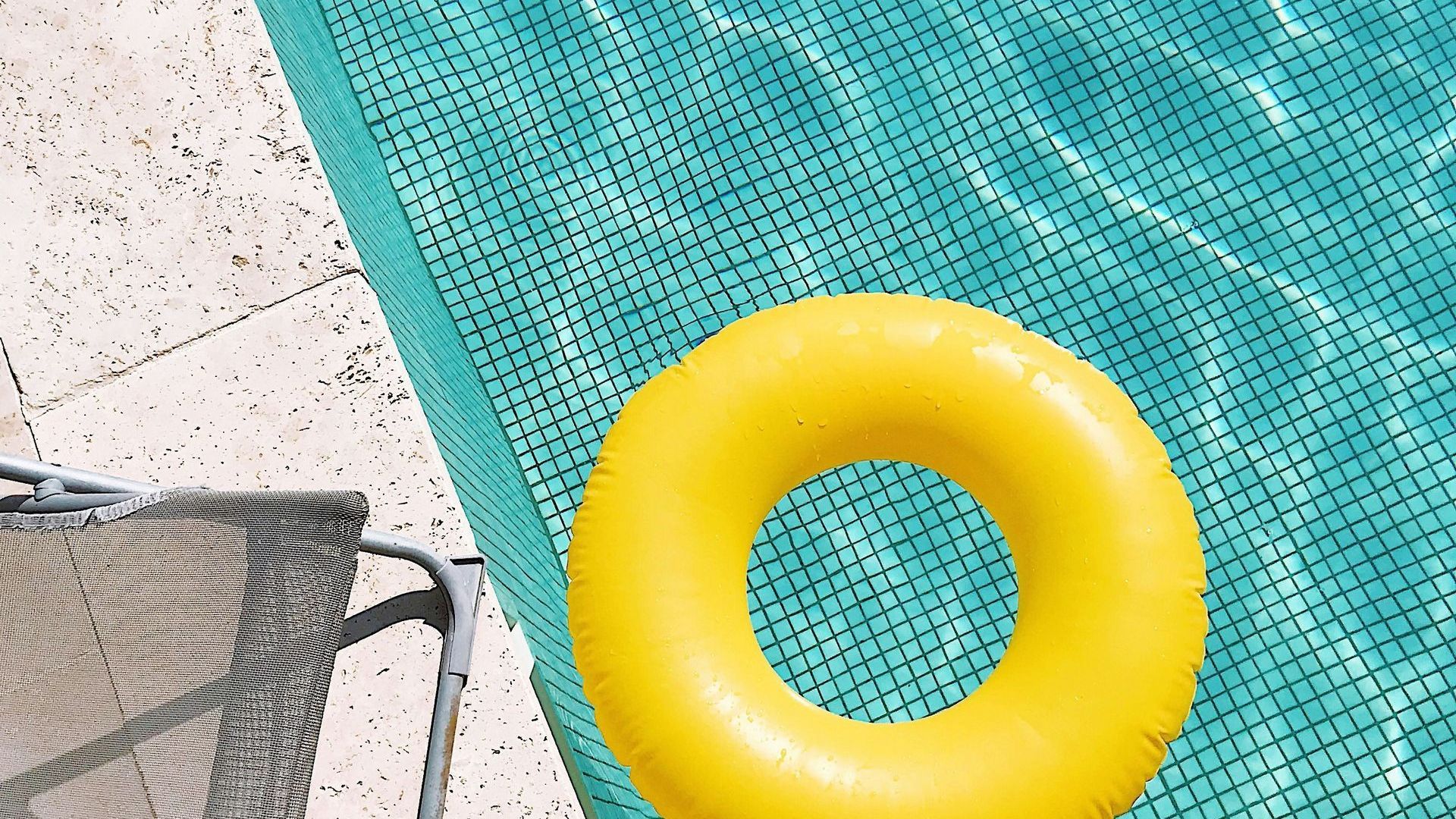 A yellow inflatable is floating in a swimming pool next to a chair.