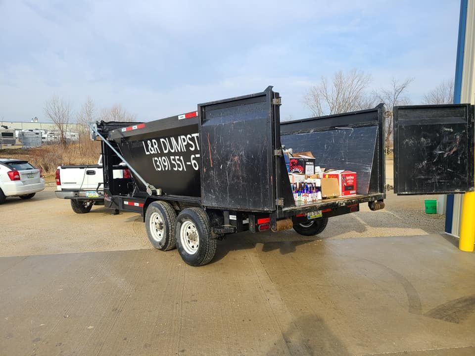 Black dumpster trailer with open rear doors, parked near a building.