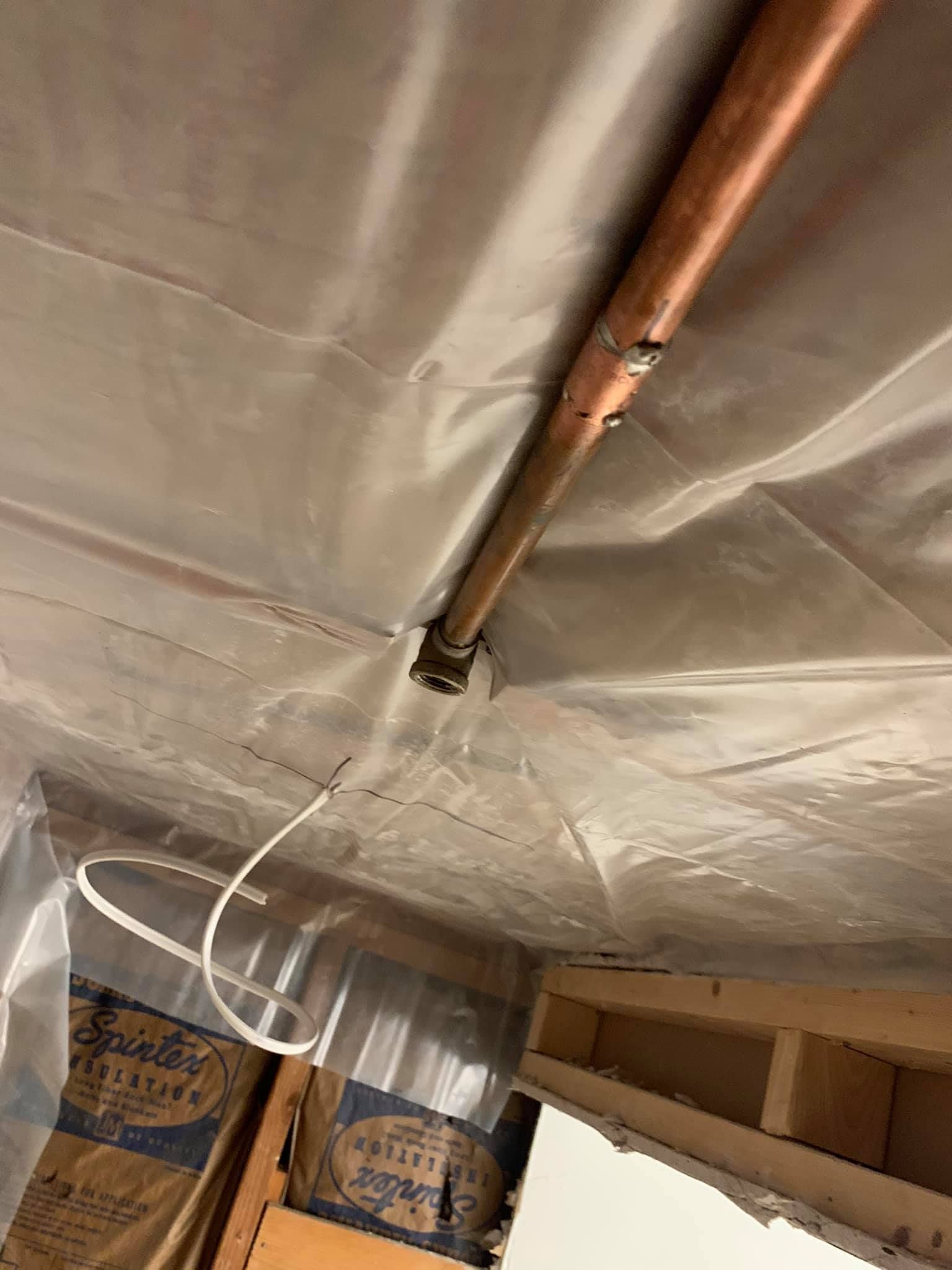 Copper pipe with joint, wrapped in plastic, in a crawlspace with insulation and wood framing visible.