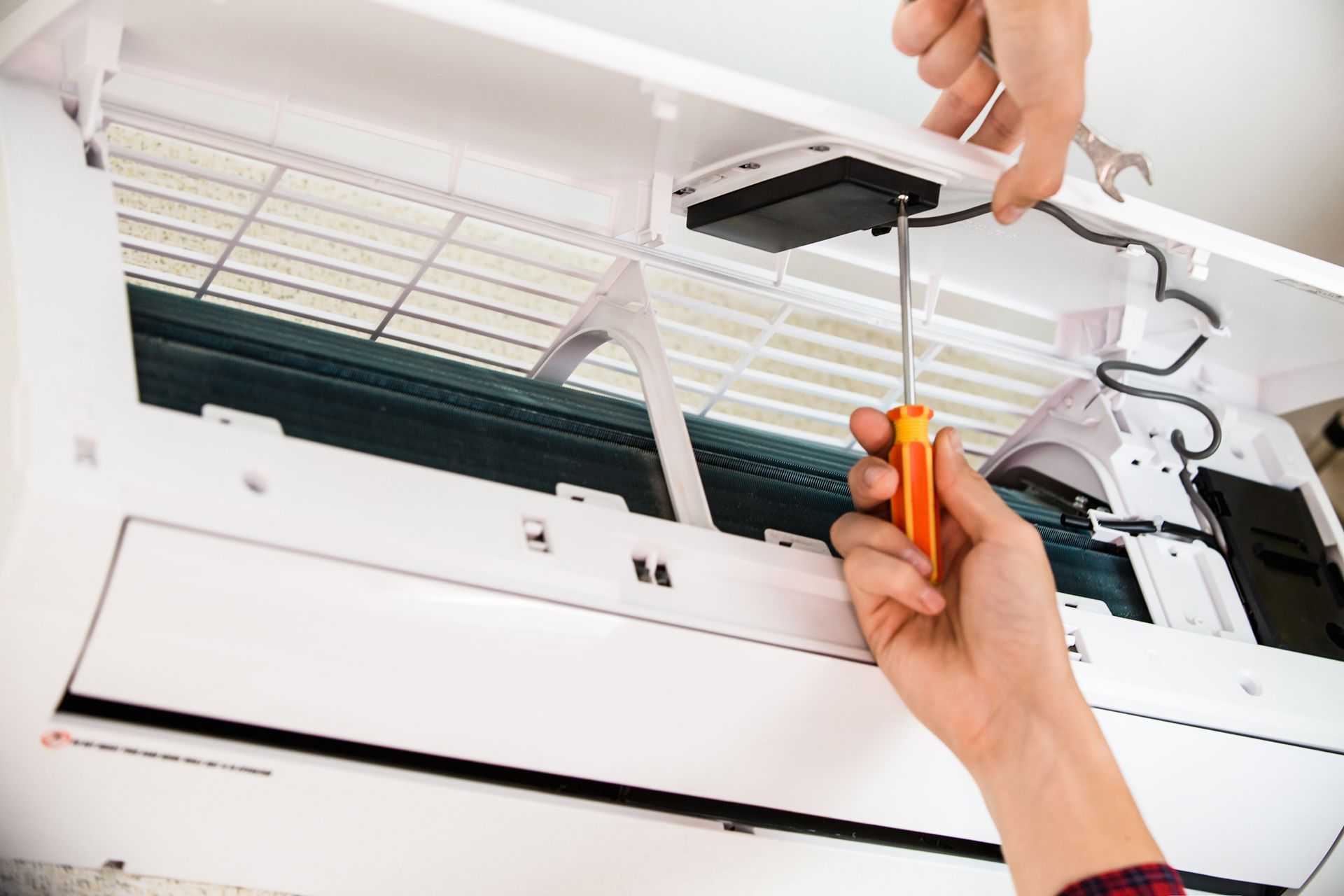 Technician using a screwdriver on an open wall-mounted AC unit during air conditioning repair work.