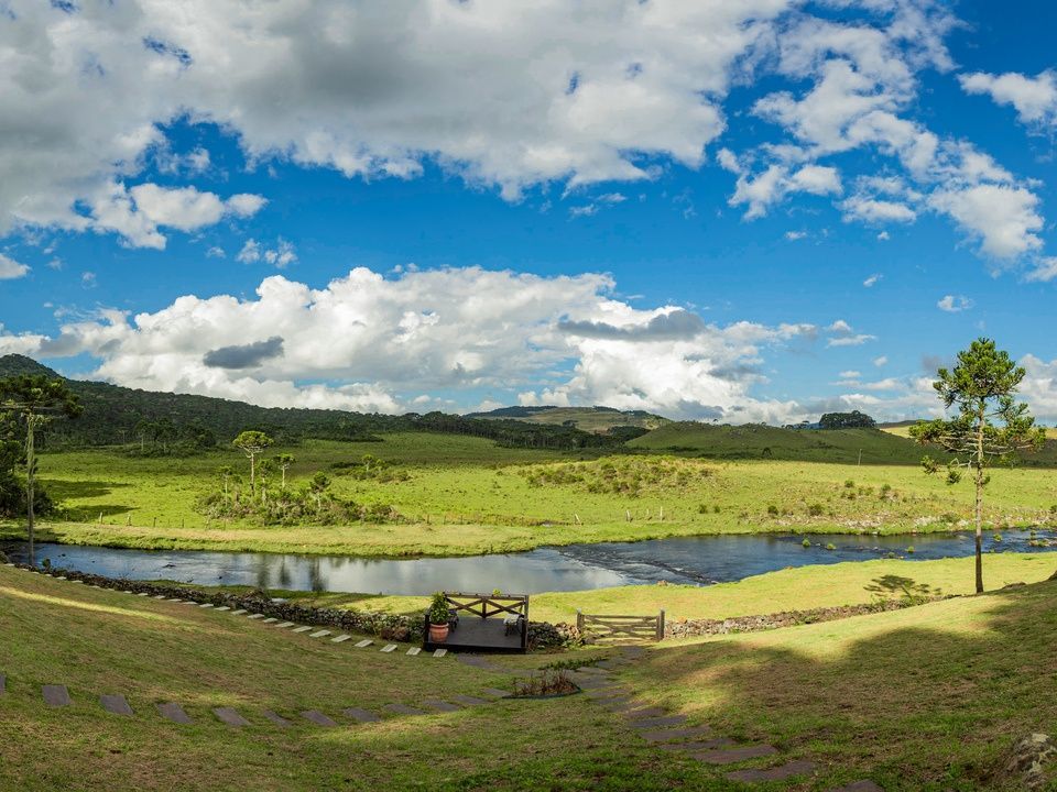 Paisagem verde com lagoa sob um céu azul brilhante com nuvens fofas.