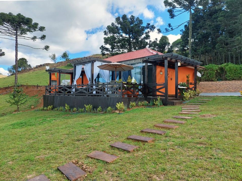 Cabana com detalhes em laranja e telhado vermelho, em uma encosta gramada. Uma passarela de madeira leva a uma varanda.