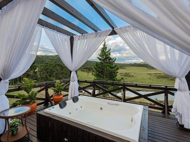 Jacuzzi ao ar livre em um deck de madeira com cortinas brancas, com vista para uma paisagem deslumbrante.