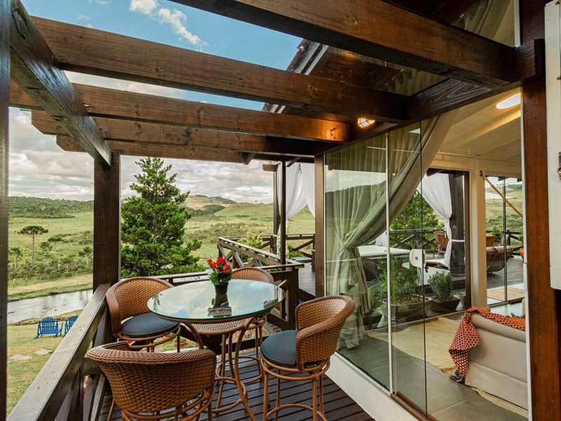 Pátio externo com mesa e cadeiras, com vista para uma paisagem verdejante e um corpo d'água.
