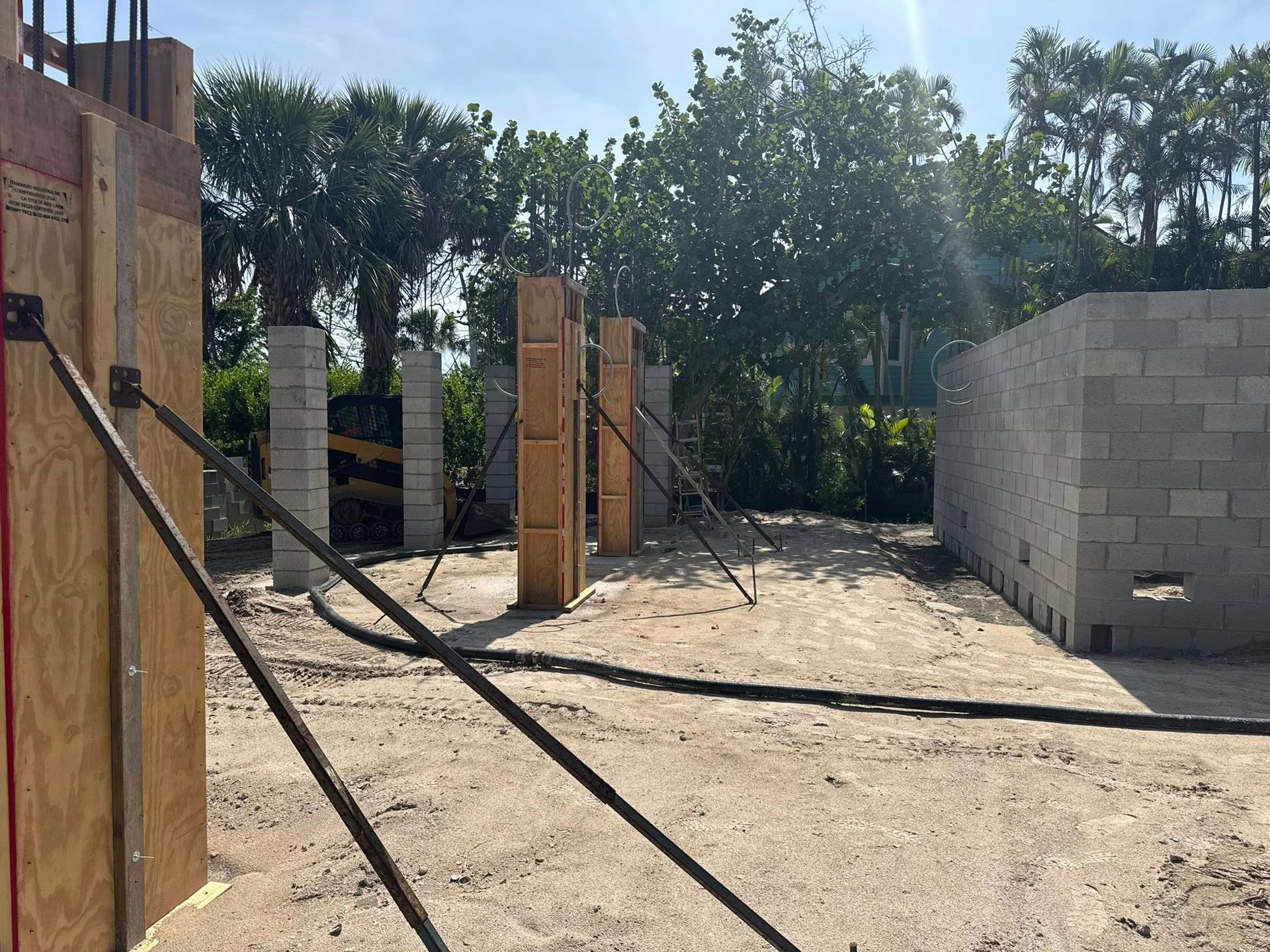 Construction site with wooden forms, cinder block wall, and support braces on sandy ground.