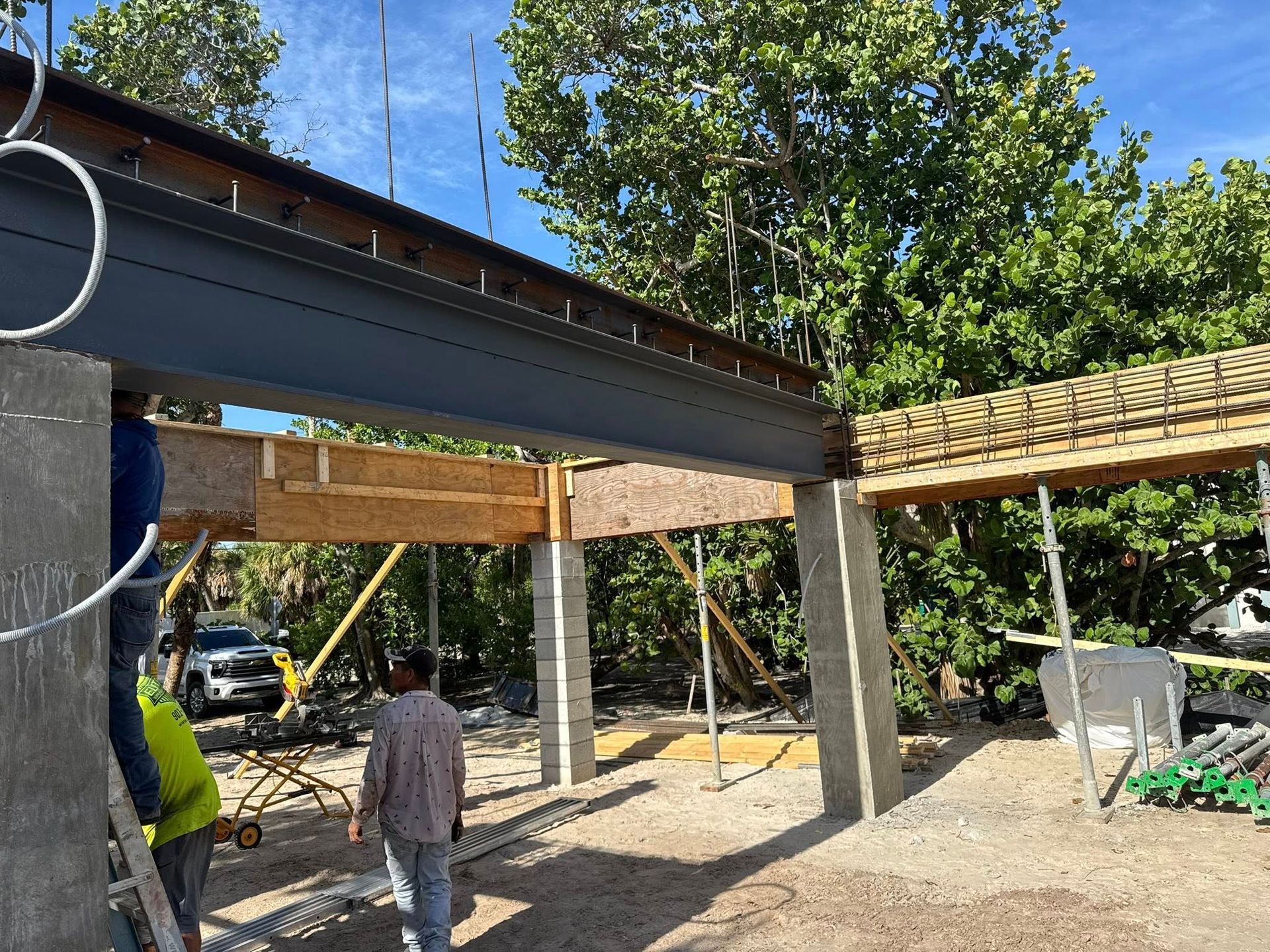 Construction site with steel beams, wooden framing, and two workers under a partially built roof.