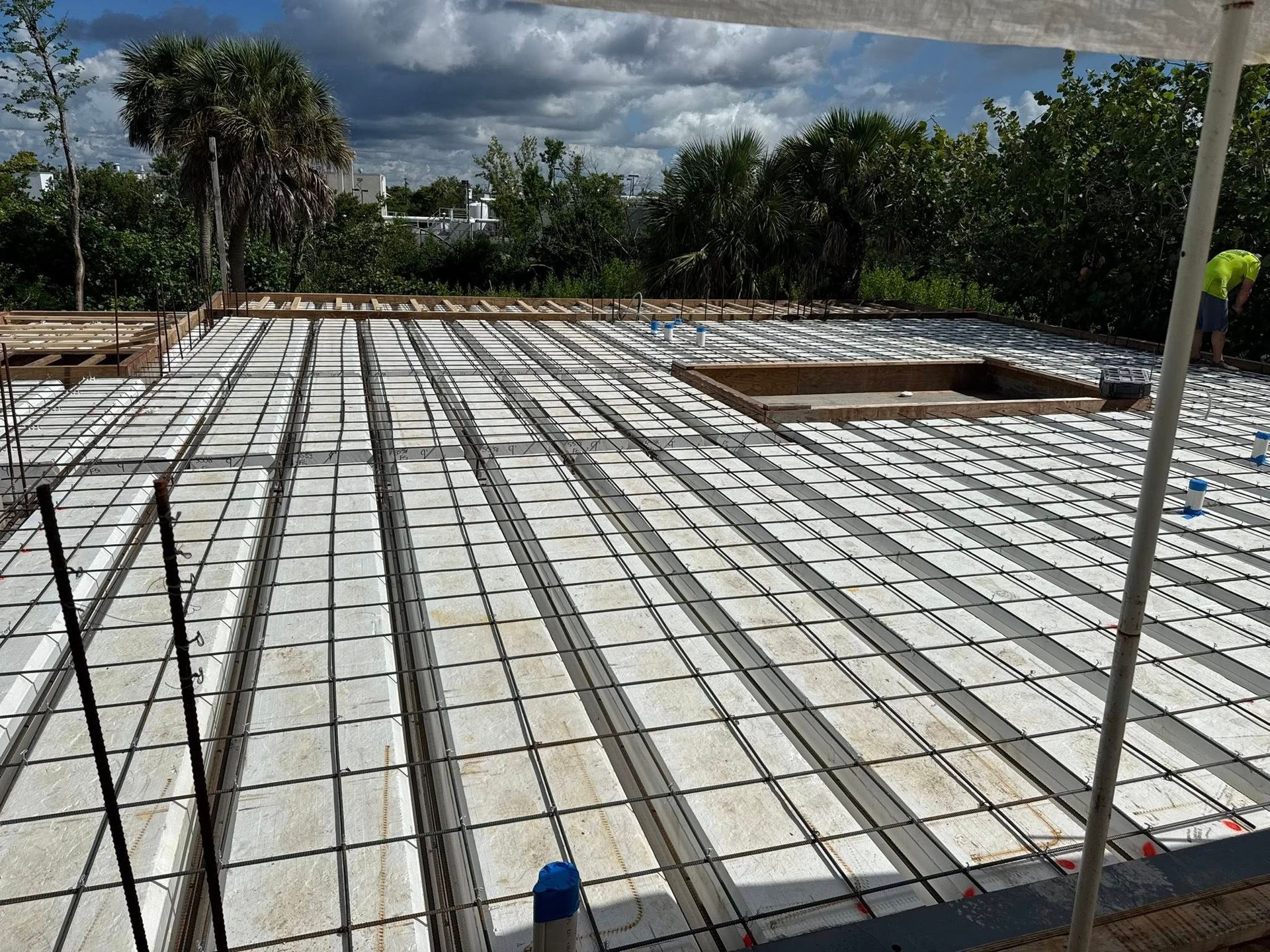 Concrete foundation with white grid formwork at a construction site under a cloudy sky