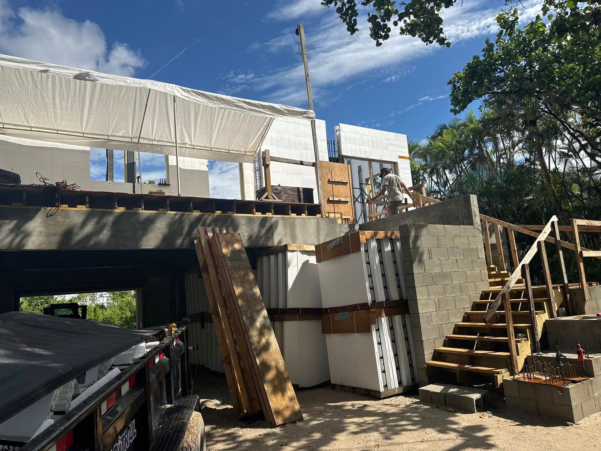 Elevated house under construction with wood framing, stairs, and scaffolding in bright daylight