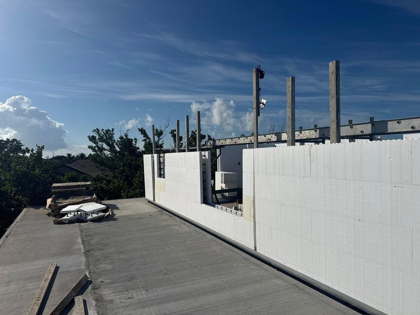 Rooftop construction site with white walls, concrete floor, and steel posts under a blue sky.