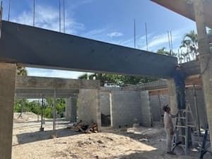 Partially built concrete structure with workers, ladder, and exposed beams under a bright sky