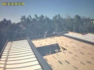 Rooftop under construction with a skylight opening, surrounded by trees in daylight.