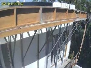 Rusted metal bridge structure with diagonal support beams over a concrete wall, viewed from below.