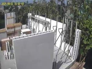 Outdoor construction site with white walls, scaffolding, and stacked materials under bright sunlight.