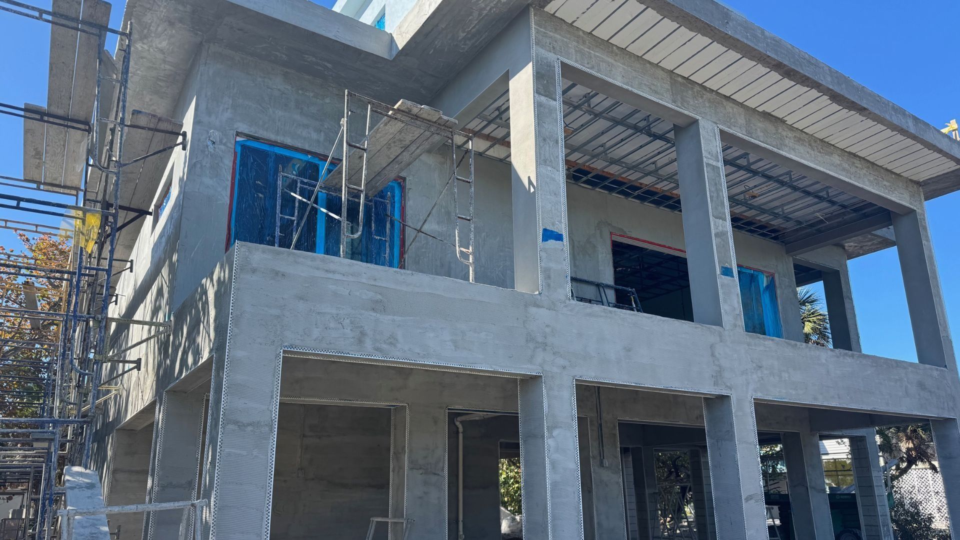 Concrete two-story house under construction with unfinished balconies and blue temporary fencing