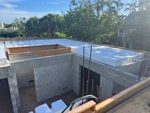 Concrete building under construction with flat roof framing, ladders, and blue sky in the background
