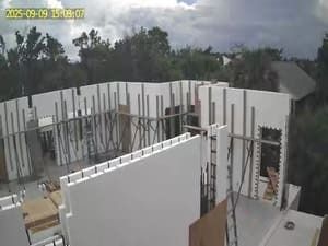 Construction site with white wall panels and exposed steel framing under a cloudy sky