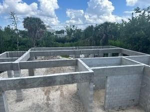 Concrete foundation walls of a house under construction in a grassy outdoor area under a cloudy sky