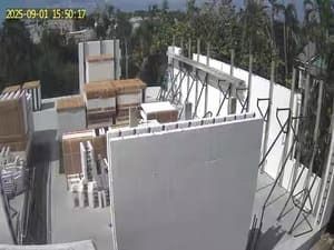 Rooftop construction site with white walls, scaffolding, stacked materials, and palm trees in the background