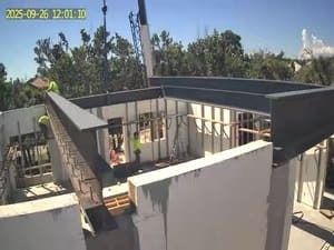 Construction site with white walls and black roof framing under blue sky