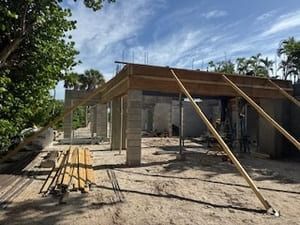 Partially built concrete house with wooden roof supports and lumber on a sunny construction site