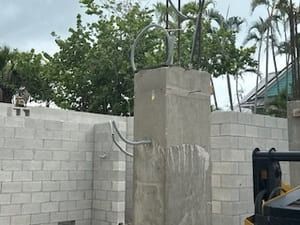 Concrete wall under construction with a central column and exposed rebar, surrounded by trees and scaffolding