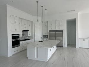 Bright white modern kitchen with an island, built-in appliances, and light wood flooring