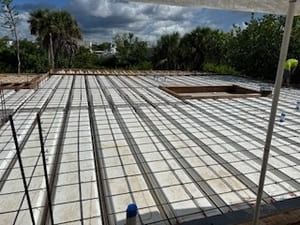 Concrete slab foundation under construction with rebar grid and wooden forms outdoors under cloudy sky