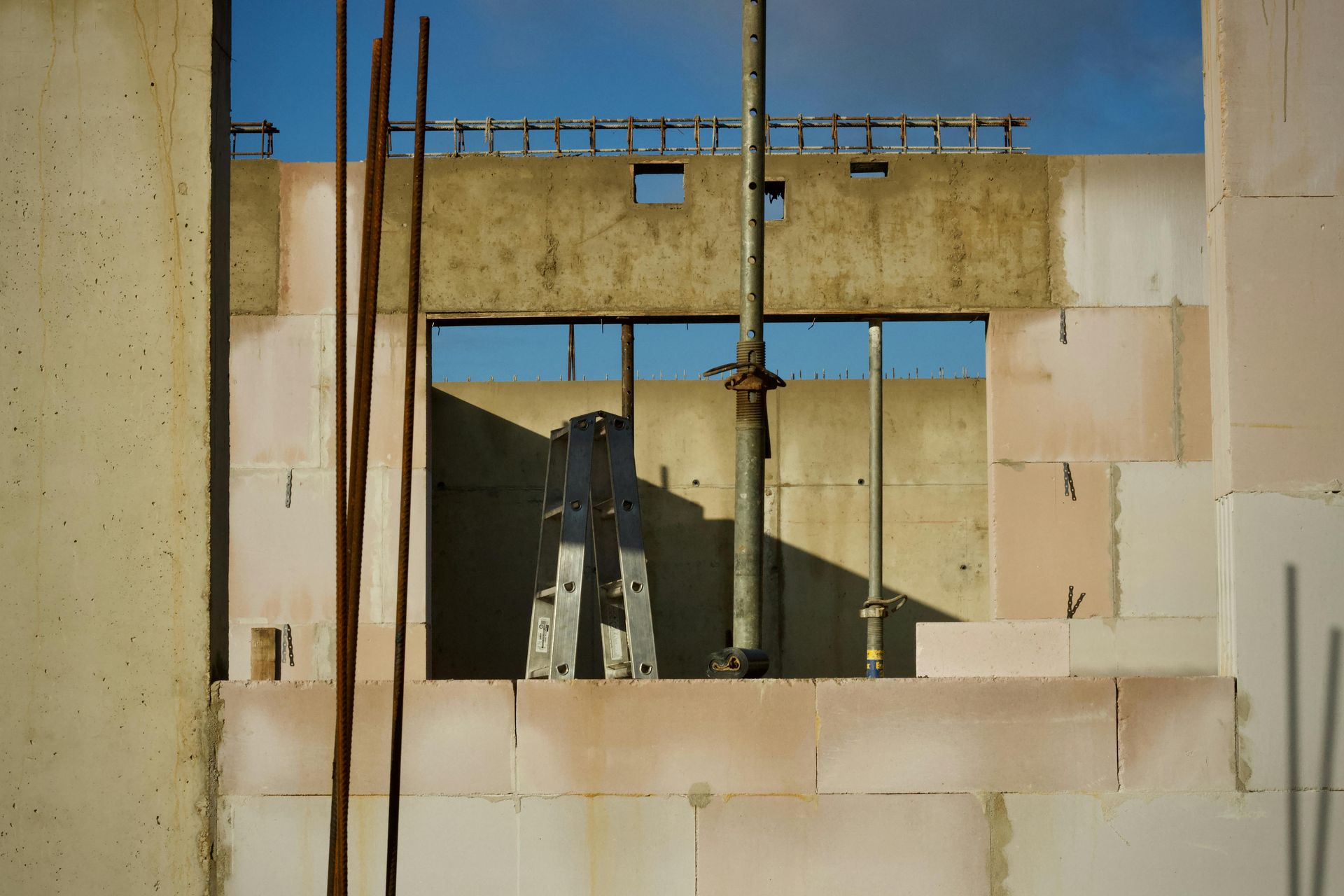 Ruined concrete wall with rectangular openings, pipes, and blue sky visible through the structure
