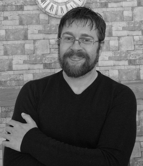A man with a beard is smiling in a black and white photo.