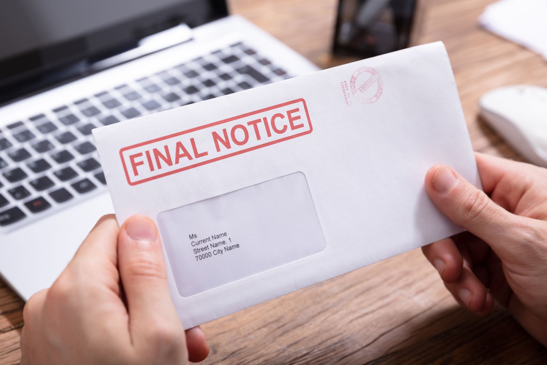 A person is holding a final notice envelope in front of a laptop.