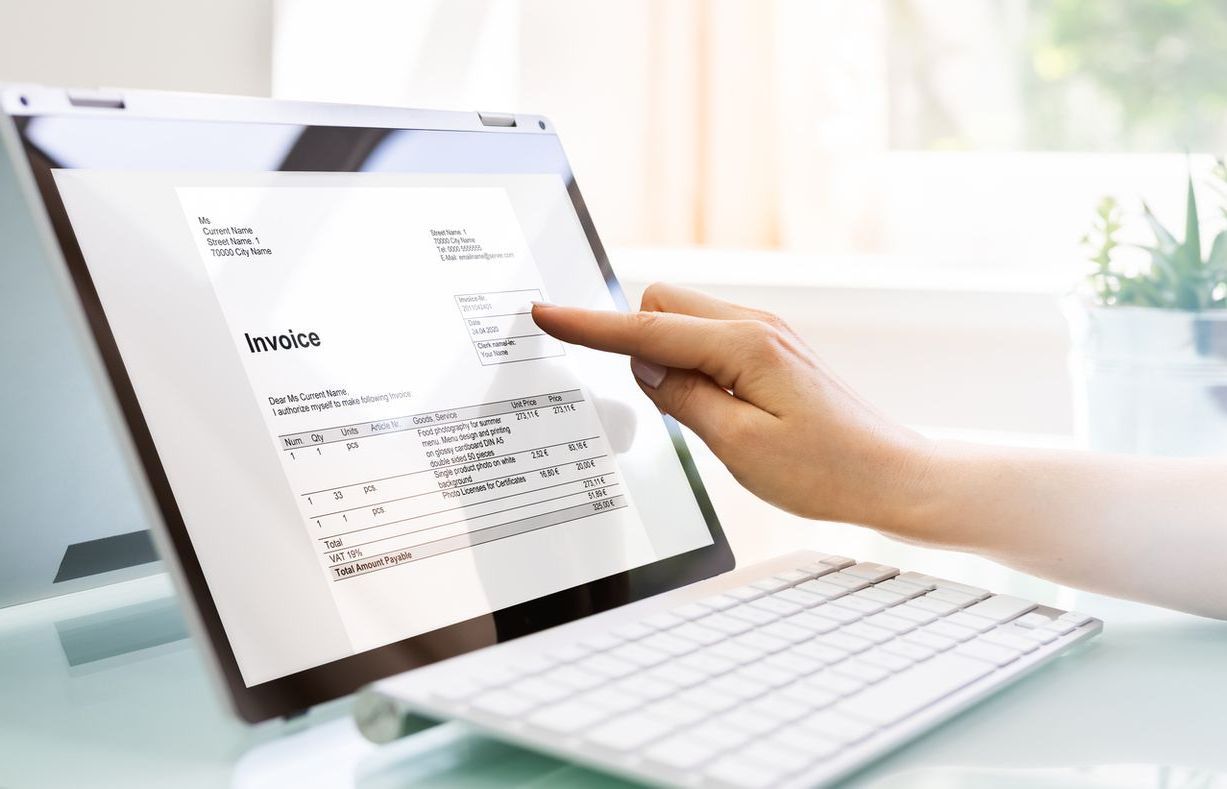 A person is pointing at an invoice on a laptop computer.