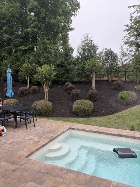 Backyard pool with stone patio, outdoor table, umbrella, and landscaped hillside