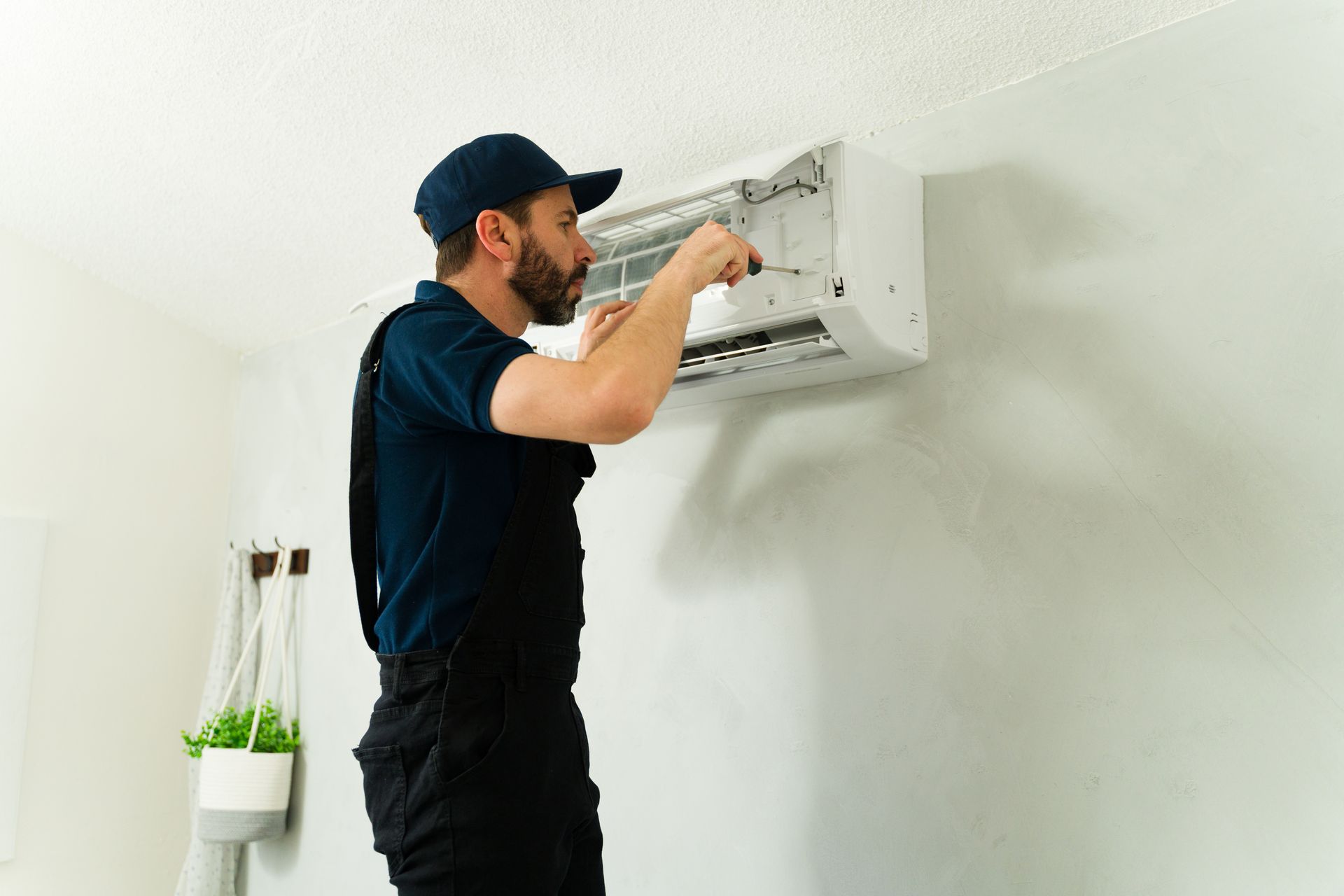 Technician repairing a wall-mounted air conditioning unit indoors. Technician repairing a wall-mounted air conditioning unit indoors.